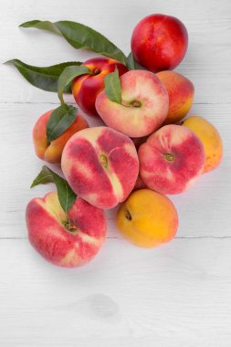 Beyaz ahşap zemin üzerine yeşil yaprakları ile birçok çeşitleri ile kompozisyon şeftali. üstten görünüm