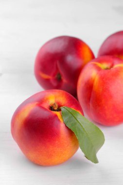 Beyaz ahşap zemin üzerine yeşil yaprak yakın çekim ile Olgun büyük nektarin