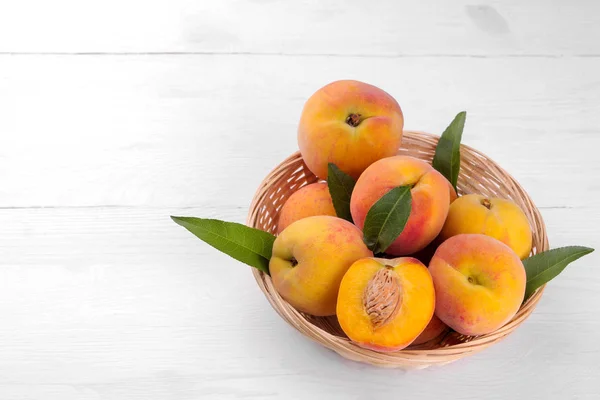 Ripe big peach in a basket on a white wooden background close-up. with place for inscription