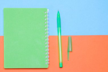 Yeşil defter ile parlak çok renkli arka plan üzerinde yeşil bir kalem. Okul malzemeleri. Üstten görünüm