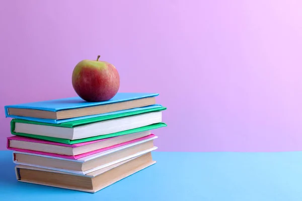 Many colorful books and an apple on a bright multi-colored blue and pink background. School supplies.