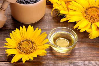 kahverengi ahşap zemin üzerine sarı parlak ayçiçeği yanındaki bir cam kasede ayçiçek yağı