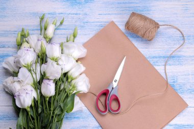 Beyaz buket güzel bir mavi ahşap arka plan üzerinde ambalaj kağıt makas ve ip ile çiçek eustoma