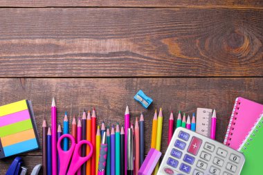 Çeşitli renkli okul ve ofis malzemeleri üzerinde kahverengi ahşap bir masa. üstten görünüm