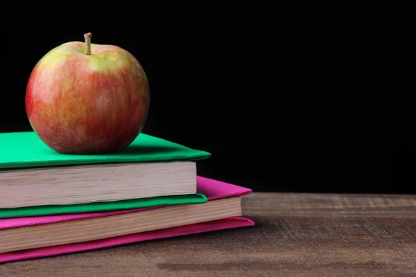 Books and an apple on a brown wooden table on a black background. concept of education