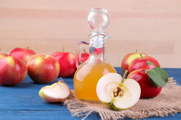 Apple vinegar next to fresh red apples on a blue table on a natural wooden background