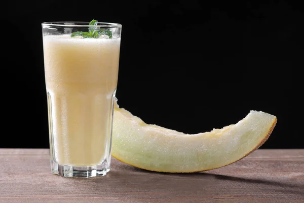 Smoothies of melon next to a slice of melon on a brown wooden table on a black background
