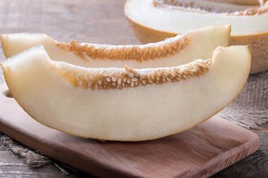 Kahverengi ahşap bir masa üzerinde bir kesme tahtası üzerinde taze olgunlaşmış kavun parçaları