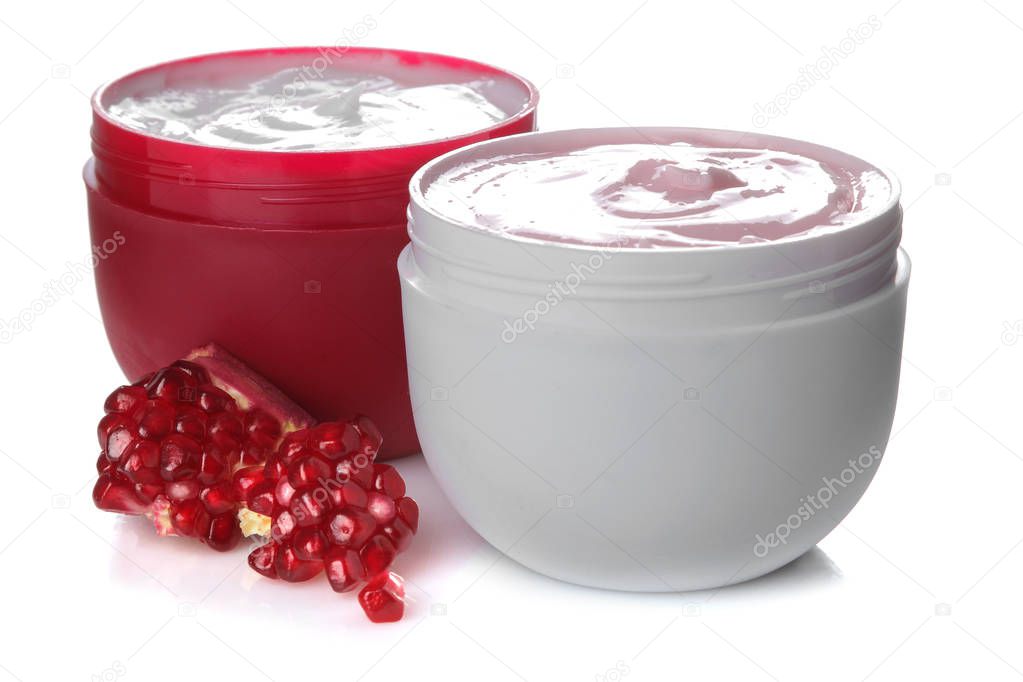 Cream in a white and red jar next to fresh pomegranate on a white isolated background