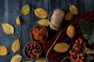 Badem kuru kayısı ve sıcak eşarp ve sarı sonbahar aranjmanı koyu mavi ahşap bir masa üzerinde bırakır. üstten görünüm