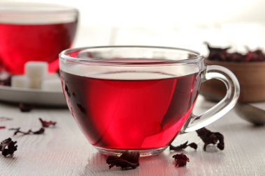 Beyaz ahşap bir masa üzerinde kuru çay ile cam bardak sıcak kırmızı pembe çay