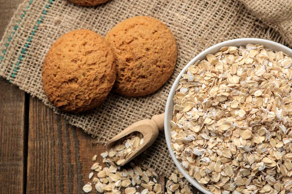 Dry oatmeal and oatmeal cookies in a white bowl and a wooden spoon. food. healthy food. on a brown wooden table.