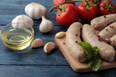 Domates, sarımsak, tereyağı ve fesleğen yemek pişirmek için malzemelerle çiğ sosis. üzerinde mavi bir ahşap masa.