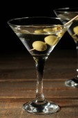 Martini v skleněné sklenici s zelenými olivami na jehle na hnědý dřevěný stůl. koktejly. Bar