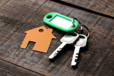 Bir ev satın alma kavramı. Tuşları ile bir Anahtarlık ve kahverengi ahşap arka plan üzerinde bir ev.