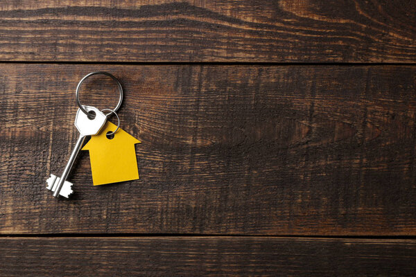 Концепция покупки дома. Ключи с брелоком дом на коричневом деревянном фоне. Вид сверху. с местом для надписи

