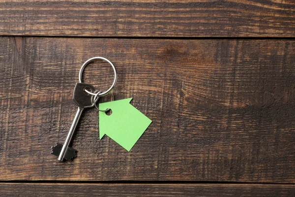 The concept of buying a home. Keys with keychain house on a brown wooden background. view from above. with space for inscription