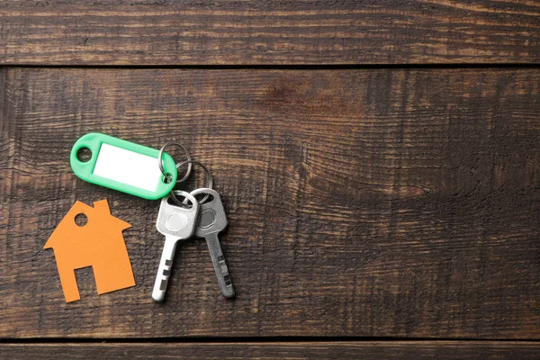 The concept of buying a home. Keys with a keychain and a house on a brown wooden background. top view with space for inscription