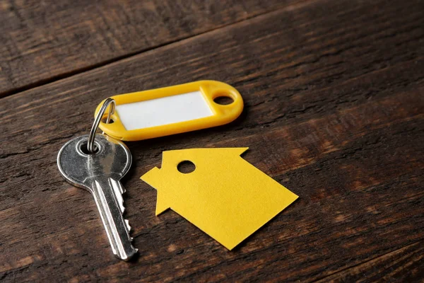 The concept of buying a home. Keys with a keychain and a house on a brown wooden background.