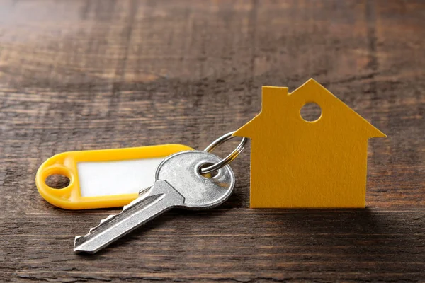 The concept of buying a home. Keys with a keychain and a house on a brown wooden background.