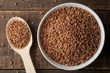 Ahşap bir kahverengi masa üzerinde bir kaşıkla karabuğday kabuğu çıkarılmış tane beyaz bir kase kuru. tahıllar. sağlıklı gıda. Yulaf lapası. üstten görünüm