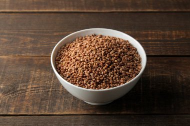 Karabuğday kabuğu çıkarılmış tane ahşap bir kahverengi masa üzerinde beyaz bir kase kuru. tahıllar. sağlıklı gıda. Yulaf lapası.