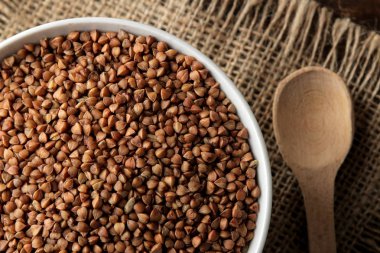 Ahşap bir kahverengi masa üzerinde bir kaşıkla karabuğday kabuğu çıkarılmış tane beyaz bir kase kuru. tahıllar. sağlıklı gıda. Yulaf lapası. üstten görünüm