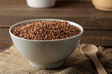 Ahşap bir kahverengi masa üzerinde bir kaşıkla karabuğday kabuğu çıkarılmış tane beyaz bir kase kuru. tahıllar. sağlıklı gıda. Yulaf lapası.