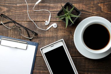 Smartphone beyaz ve bir fincan kahve gözlük ve kahverengi ahşap bir masa üzerinde bir boş. yukarıdan görüntülemek