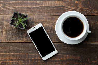 Smartphone beyaz ve kahverengi ahşap bir masa üzerinde kahve. yukarıdan görüntülemek
