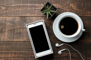 Bir fincan kahve kahverengi ahşap bir masa üzerinde ve kulaklık ile Smartphone. yukarıdan görüntülemek