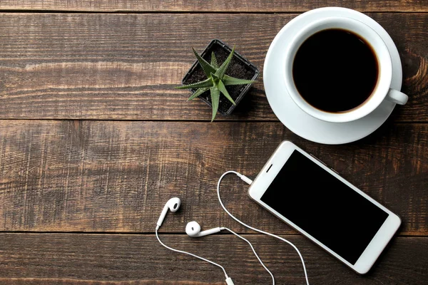 Bir fincan kahve kahverengi ahşap bir masa üzerinde ve kulaklık ile Smartphone. yukarıdan görüntülemek