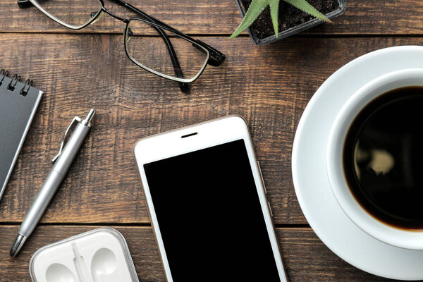 Смартфон белый и чашка с кофейными очками и блокнот на коричневом деревянном столе. вид сверху
