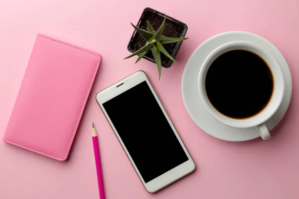 Beyaz smartphone ve bir fincan kahve ve parlak pembe bir arka plan üzerinde pembe bir not defteri. yukarıdan görüntülemek
