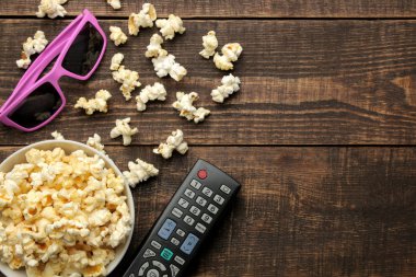 Patlamış mısır, 3d gözlük ve Tv bir kahverengi ahşap arka plan üzerinde uzak. evde film izlerken kavramı. yukarıdan görüntülemek