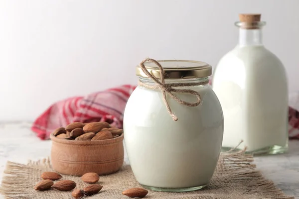 Fresh almond milk in a glass bottle and almond nuts on a light background