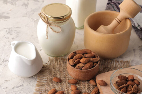 Fresh almond milk in a milk jug and almond nuts on a light background