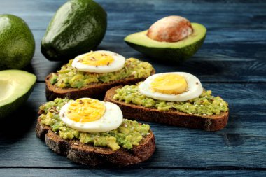 Avokado püresi ve mavi ahşap bir masa üzerinde yumurta ile sandviç. taze avokado