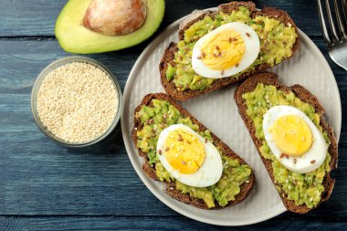 Avokado püresi ve bir tabak ve üzerinde mavi bir ahşap masa yemek pişirmek için malzemeler üzerinde yumurta ile sandviç. yukarıdan görüntülemek