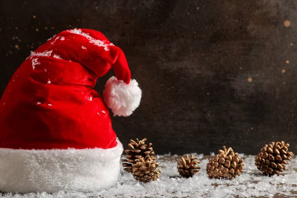 Kırmızı Santa Claus şapka ve koniler ve kar koyu kahverengi zemin üzerinde. metin için yer ile. Noel. Yeni yıl.