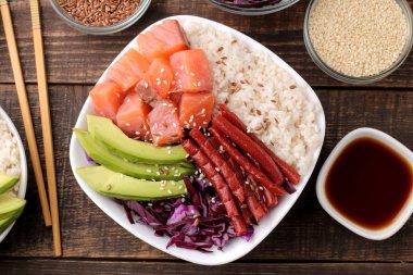 poke kase Hawaiian gıda. bir tabak pilav, somon, avokado, lahana ve peynir, susam ve soya sosu yanında. kahverengi ahşap bir masa üzerinde. üstten görünüm