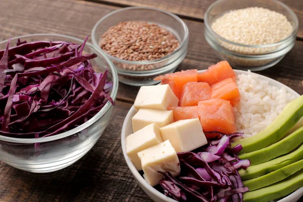 poke bowl Hawaiian food. a plate with rice, salmon, avocado, cabbage and cheese, near sesame. on a brown wooden table.