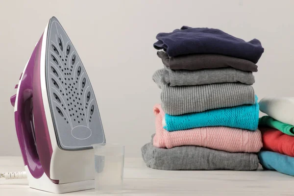 lilac iron and a stack of clothes on a light background. ironing clothes. household electrical appliances.