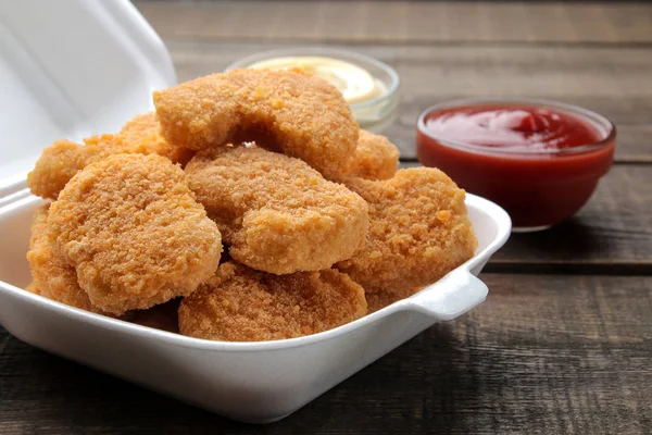 chicken nuggets in a food delivery box with white and red sauce on a brown wooden background. fast food close-up