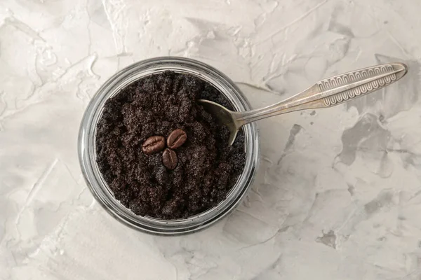 homemade coffee face and body scrub in a glass jar with a spoon on a light background. care cosmetics. view from above
