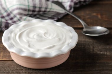 bir seramik kase kahverengi ahşap arka plan üzerine bir kaşık yanında Yunan yoğurt