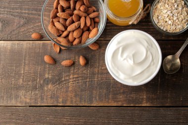 Yunan yoğurt badem ve bal, kahverengi ahşap arka plan üzerine bir kaşık yanında yulaf ezmesi seramik bir kase. sağlıklı gıda. Doğal yoğurt. Kahvaltı. metin için yer ile üstten görünüm