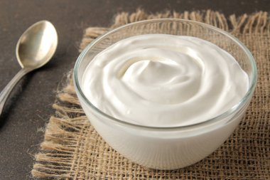 Yunan yoğurt karanlık bir arka plan üzerine bir kaşık yanındaki bir cam kabın içinde. sağlıklı gıda. Doğal yoğurt. Kahvaltı