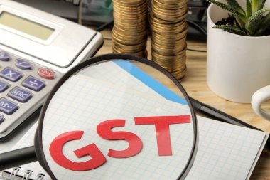 Büyüteç ve hesap makinesi, kahverengi ahşap zemin üzerinde paralar yığını altında notebook Word'de GST.
