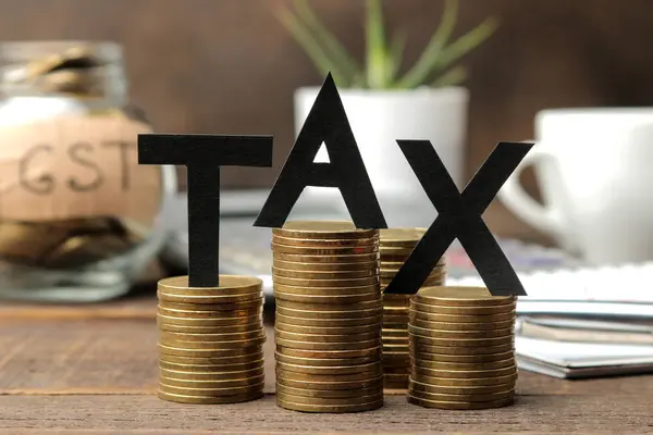 The word tax and a stack of coins with a notebook pen and coffee on a brown wooden background.